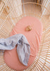 Coral Linen Bassinet Sheet with a Mist blue Linen Swaddle draped over the side of the bassinet